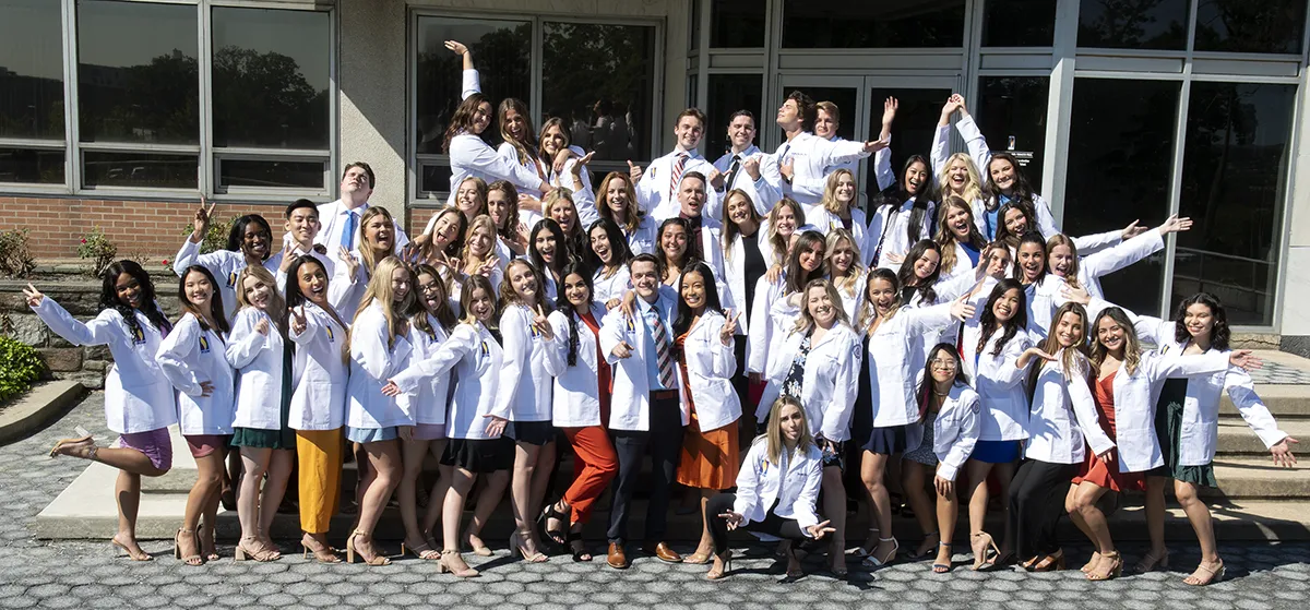 Group shot of PCOM Philadelphia physician assistant students smiling and posing in their white coats after a ceremony