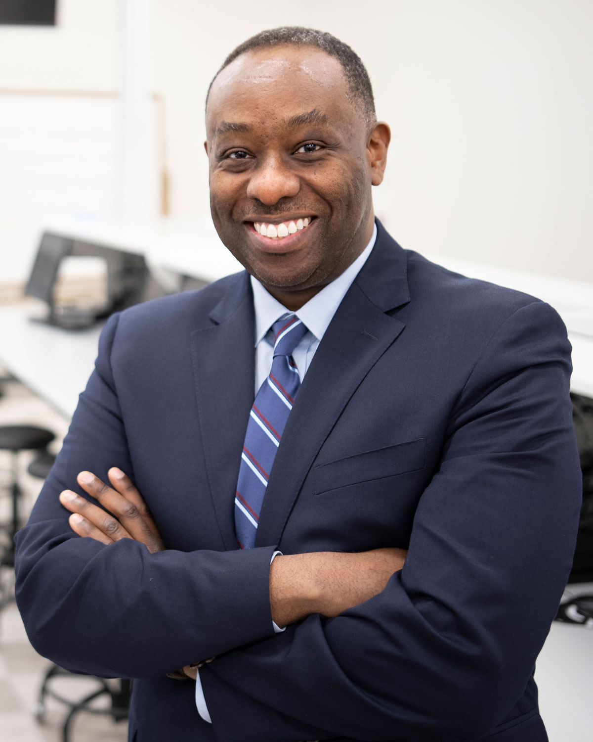 Professional headshot photograph of Shawn Spencer, RPh, PhD, dean of PCOM School of Pharmacy wearing a suit and tie in a dispensing lab
