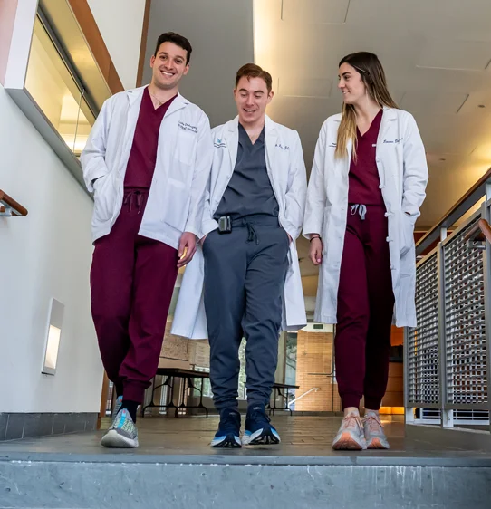 Residents in physician white coats walking and talking during a residency program at PCOM