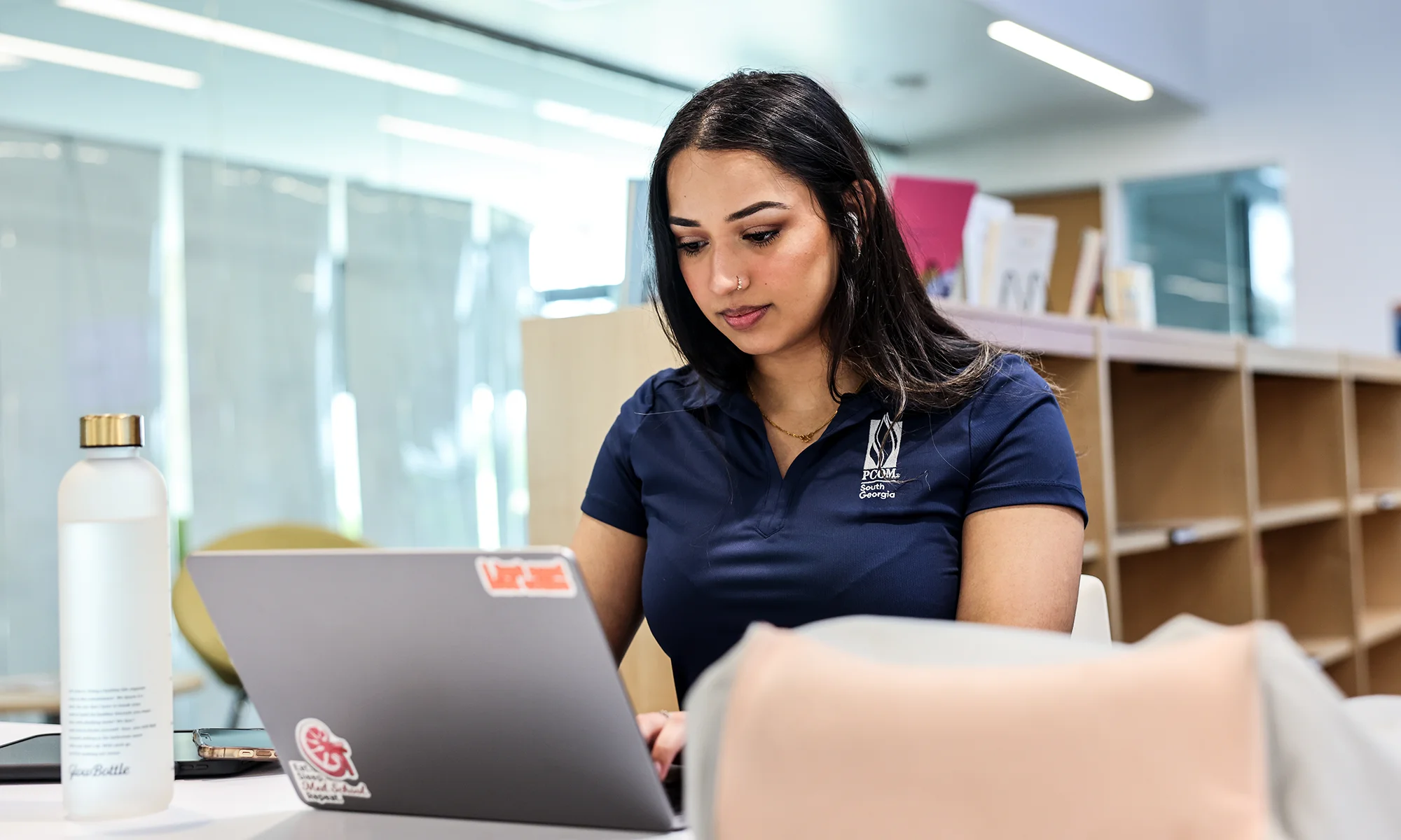 A PCOM student smiling while using a laptop to complete coursework in the Master's in Biomedical Sciences Professional Track program