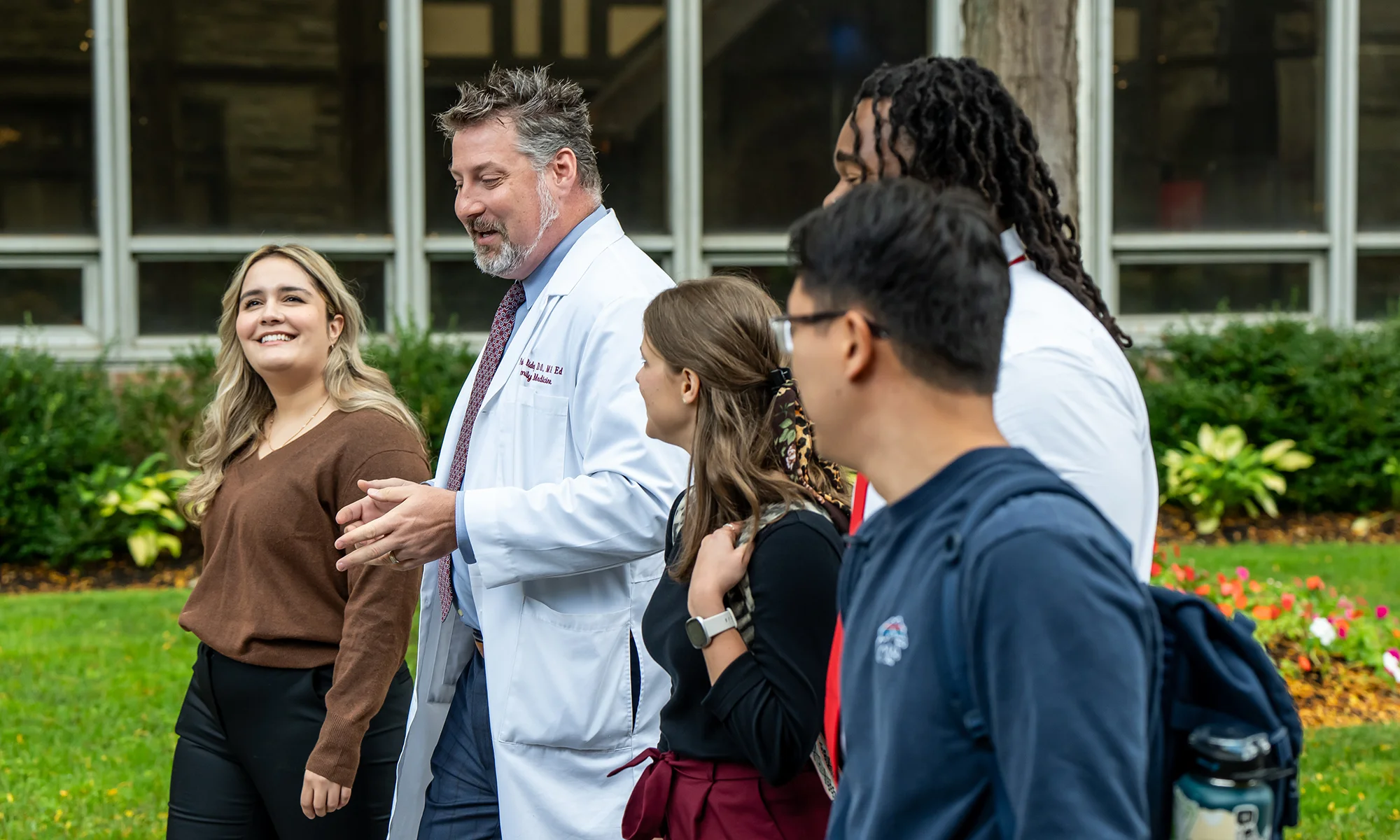 Medical students and faculty walk and talk on a path at PCOM's Philadelphia campus