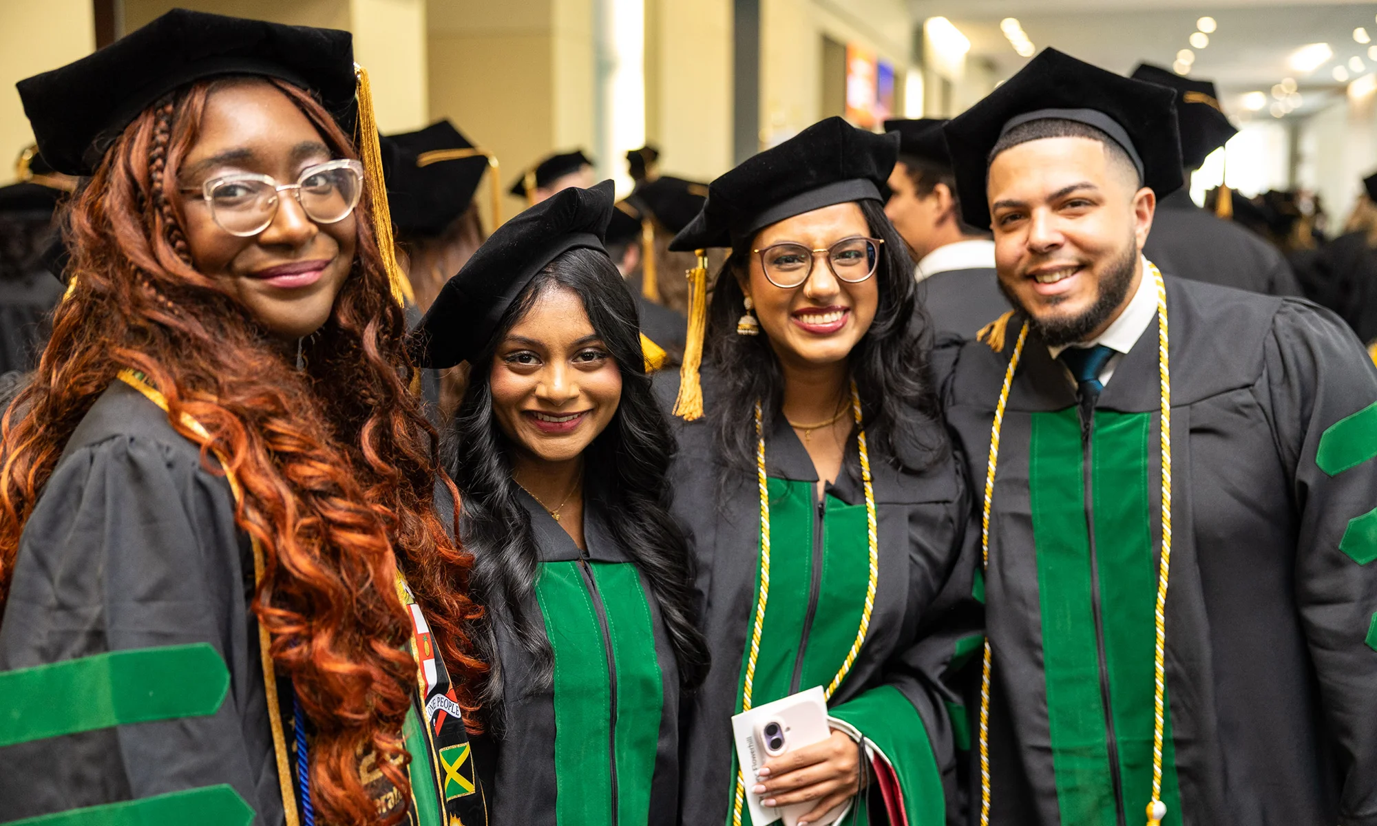 PCOM graduates wearing caps, gowns, regalia and smiling in a group photo after the commencement ceremony