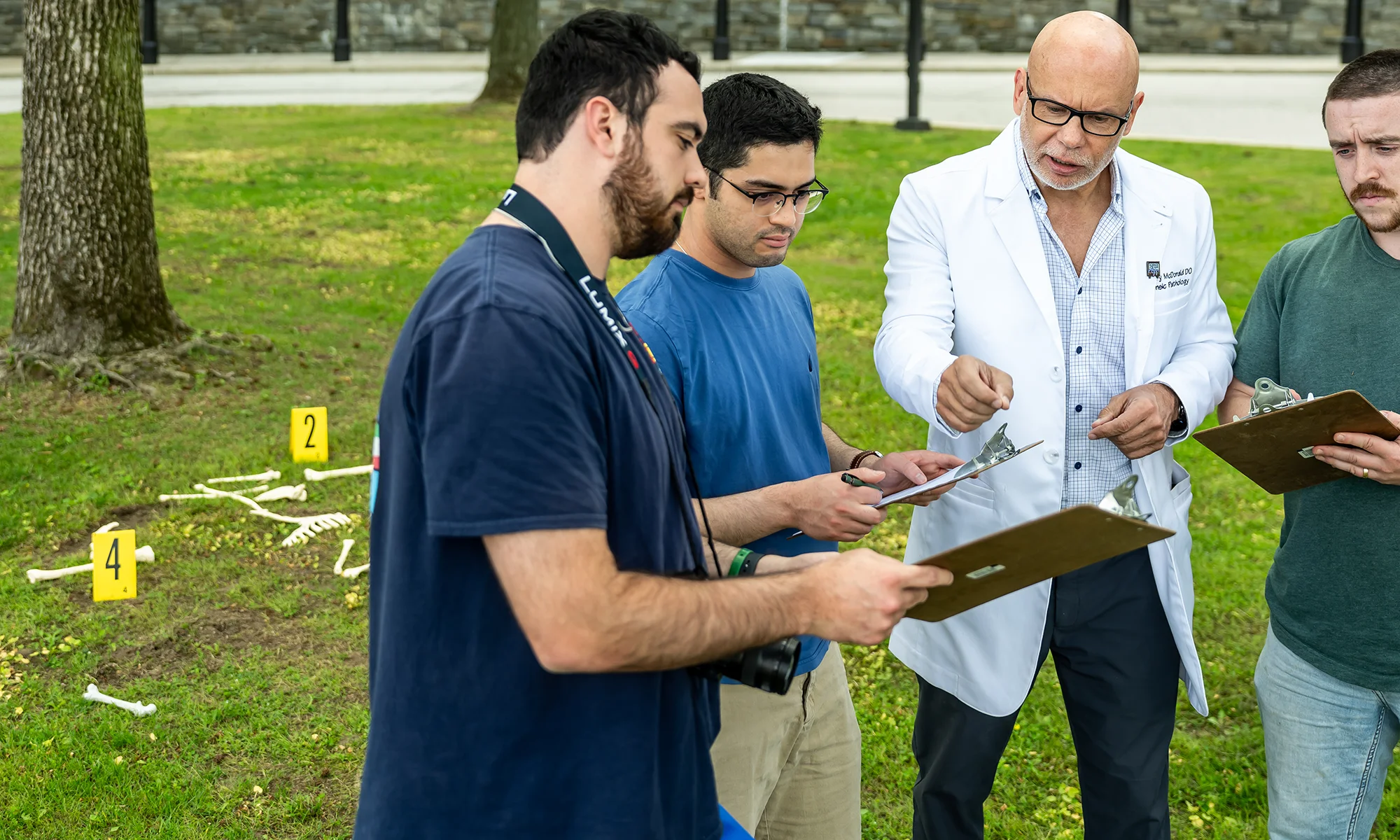 PCOM forensic medicine students and faculty reviewing notes on clipboards during a hands-on learning exercise