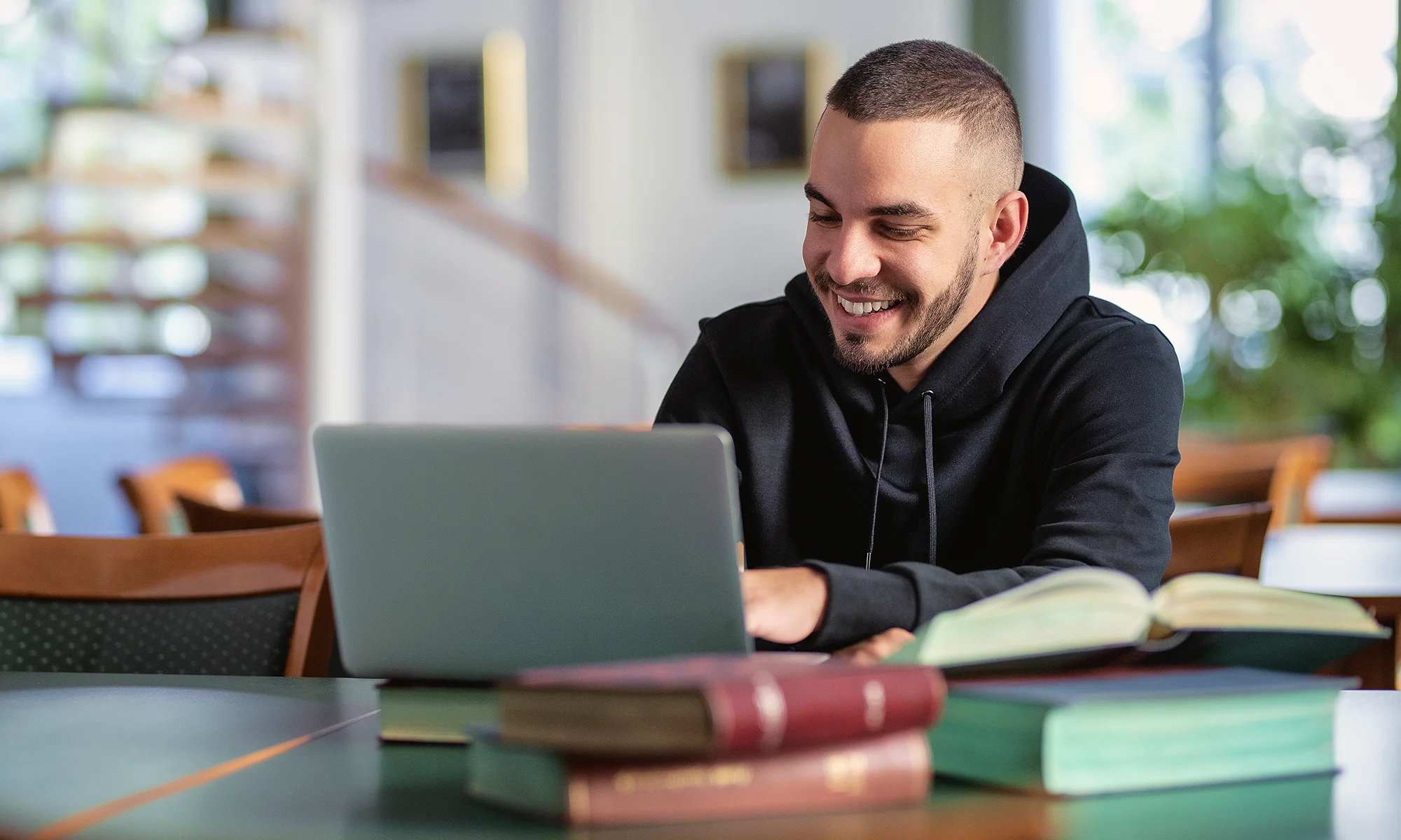 Undergrad student smiling while using laptop to take PCOM's online forensic medicine pathway course