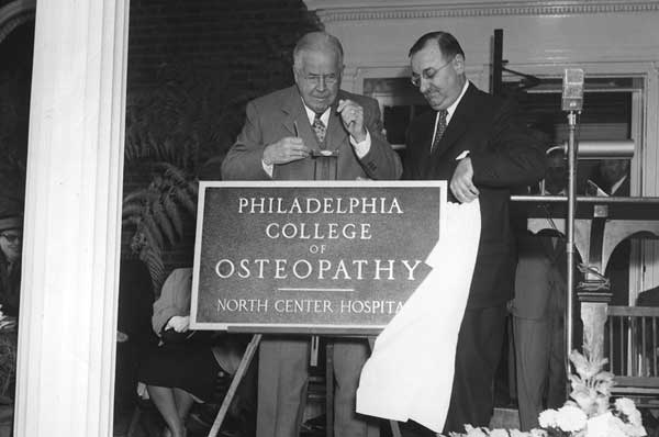 Black and white photo of college administrators revealing a building cornerstone plate