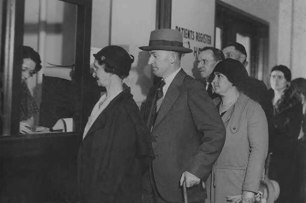 Black and white photo of patients in Depression era clothes waiting in line to be seen by medical students