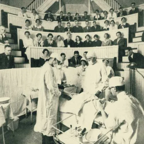 Black and white photo of medical students observing a surgery lesson in a clinical amphitheater.