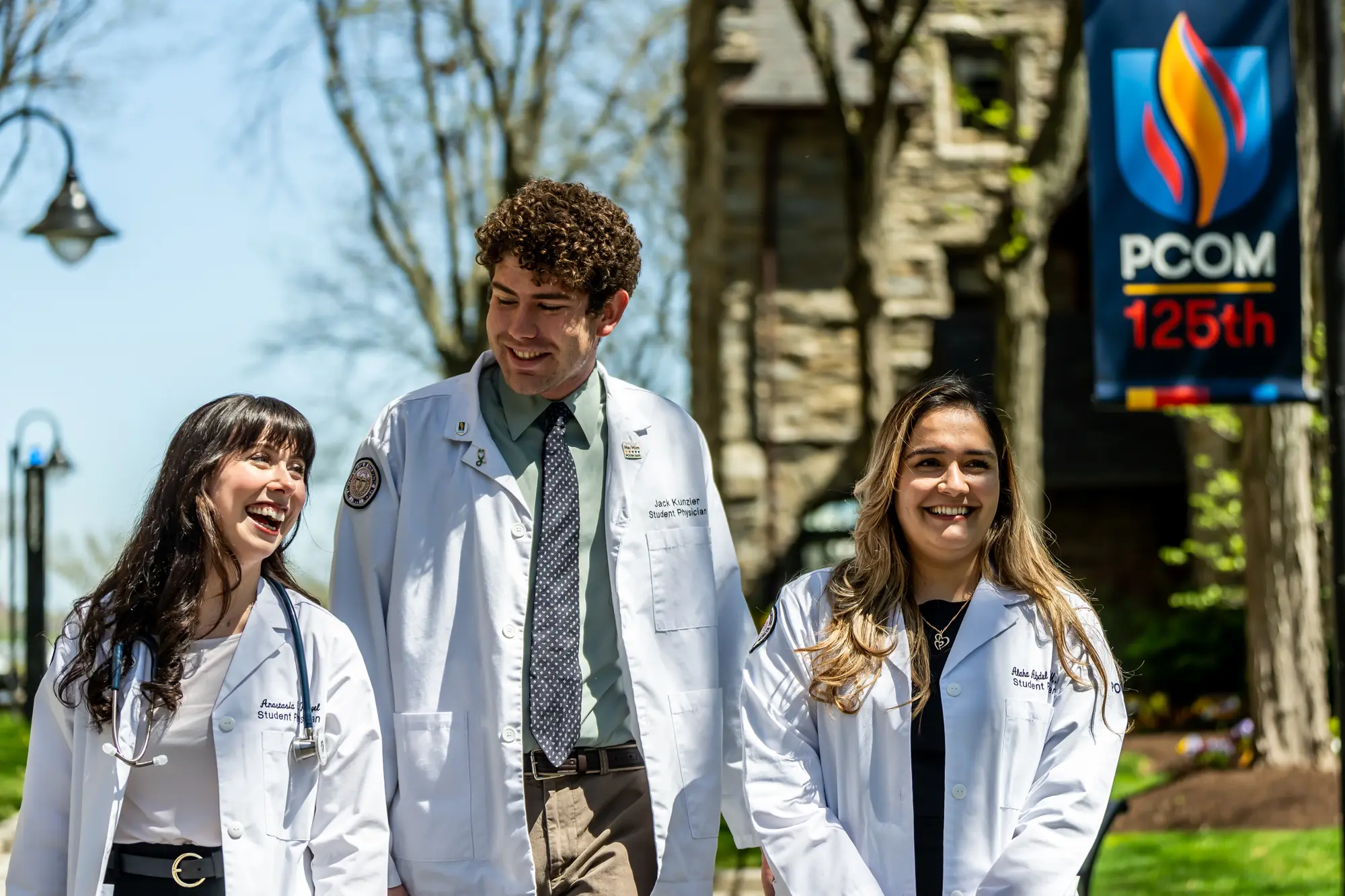 Four grad students smiling on front of the PCOM 125th anniversary collage