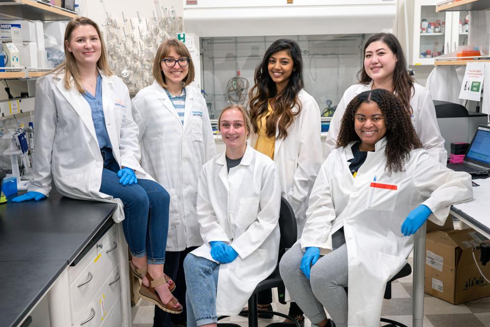 PCOM graduate and medical students smile in a group shot wearing lab coats in a research lab