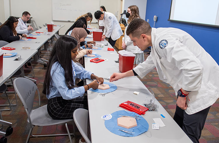 PCOM Georgia DO students show pre-med students suturing techniques in a classroom