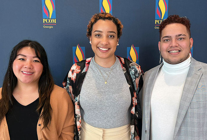 Pre-med students smile in front of a PCOM Georgia flame logo backdrop