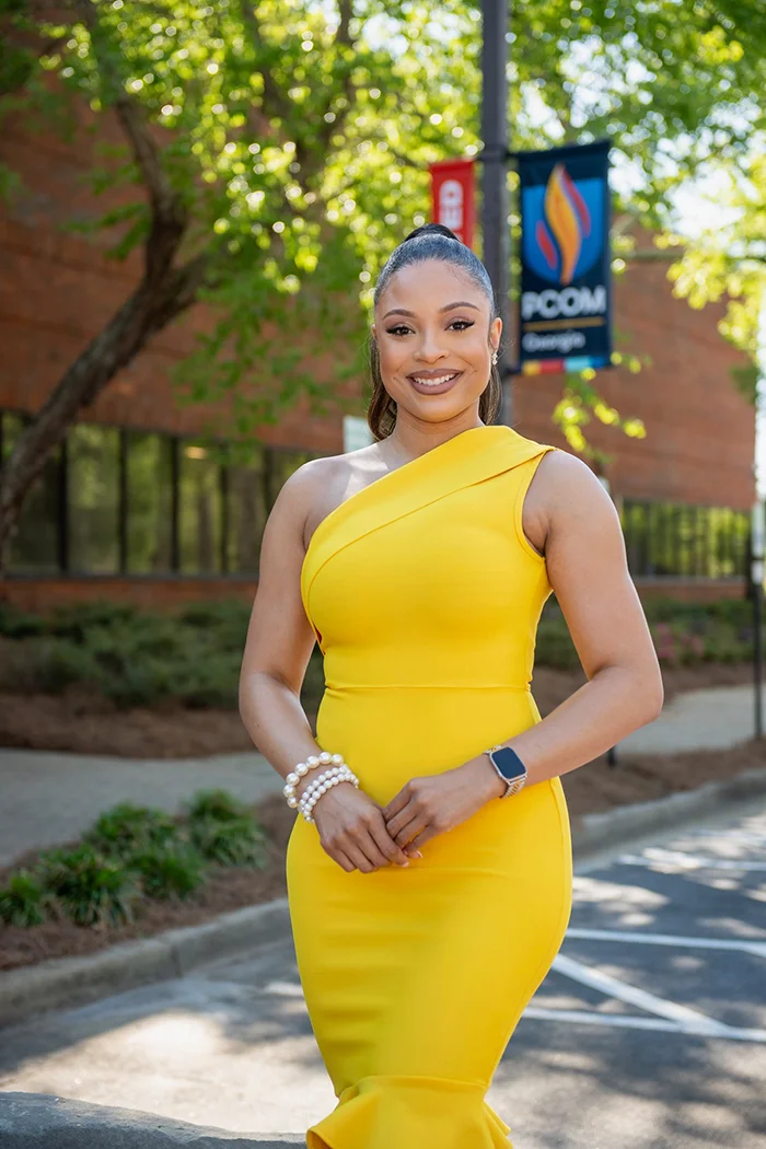 Jaelyn Benyard (PharmD ‘27) wears a yellow dress with PCOM Georgia in the background