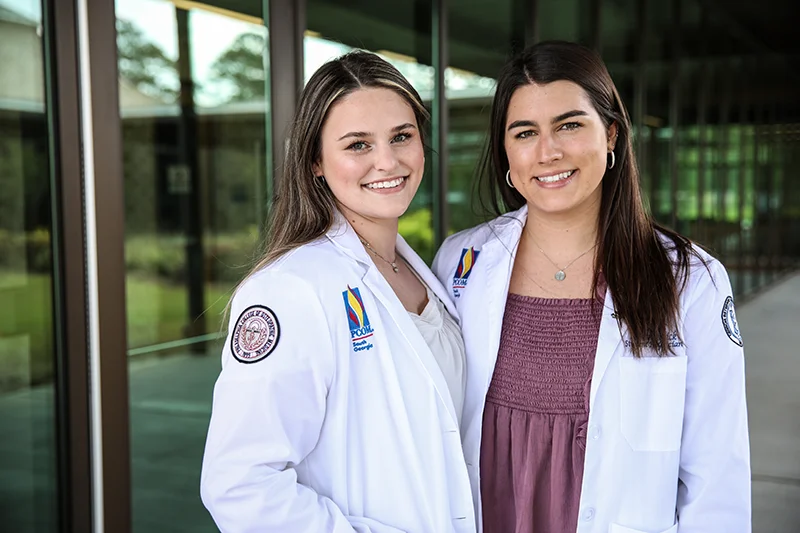 Two students in white coats standing on the patio at PCOM South Georgia