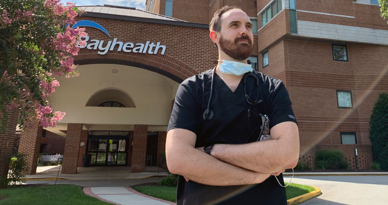 PCOM Georgia med student Christian Pruitt (DO '22) wears scrubs and stands outside a Bayhealth medical office.