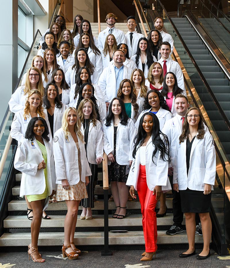 Physician assistant studies students take a group shout and smile donning their new white coats during the white coat ceremony