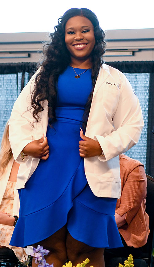 A PCOM Georgia PT student smiles on stage after receiving her white coat
