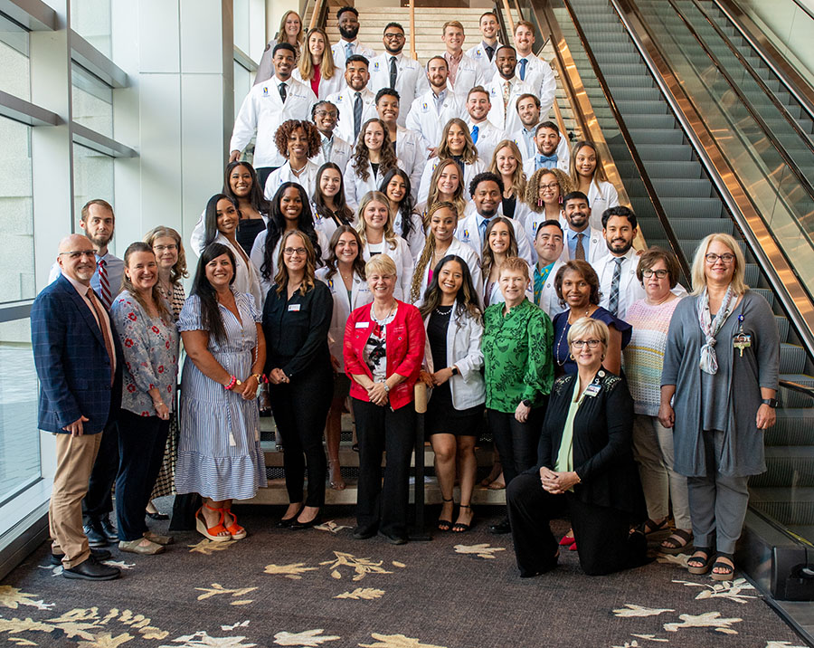 The PCOM Georgia DPT Class of 2025 poses with faculty on a stairwell following their white coat ceremony
