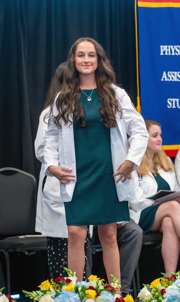 PCOM Georgia PA student Caleigh Cianci smiles as she dons her white coat on stage during the ceremony