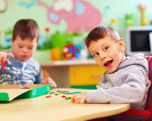 Two young children sit at a table playing with toys during elementary school