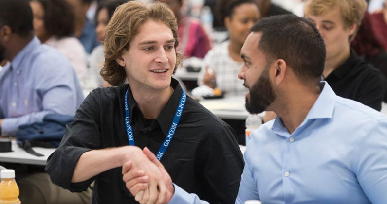 Two prospective students shake hands during an open house event.