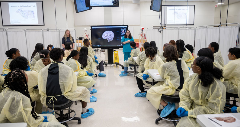 Medical students lecture in front of seated area high school students in PCOM Georgia laboratory