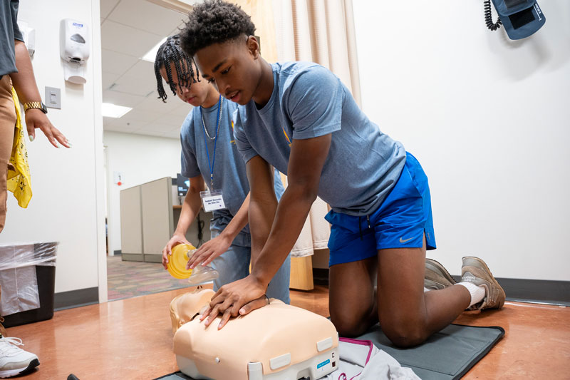 Two high school students practice CPR on a manikin