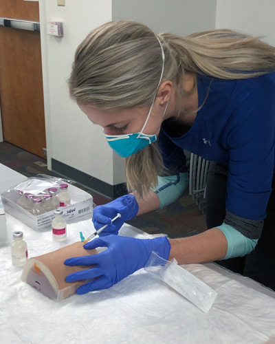 A PCOM Georgia graduate student learns how to safely inject vaccines into a mannequin arm.