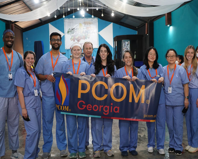 Medical students taking a photo with a PCOM Georgia banner