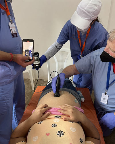 Medical students and a faculty member use a pocket ultrasound instrument to show a pregnant woman her child