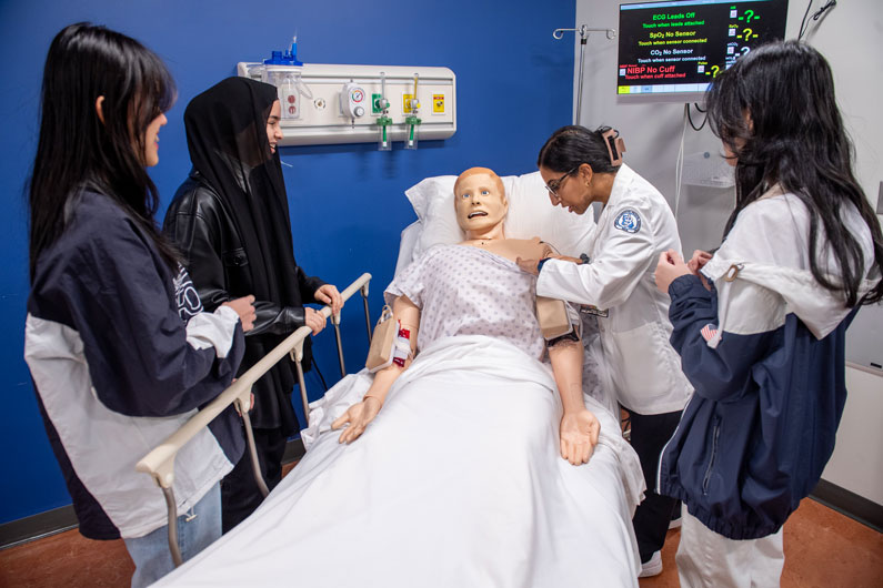 high school students observe staff member demonstrate medical procedure on simulation center mannequin