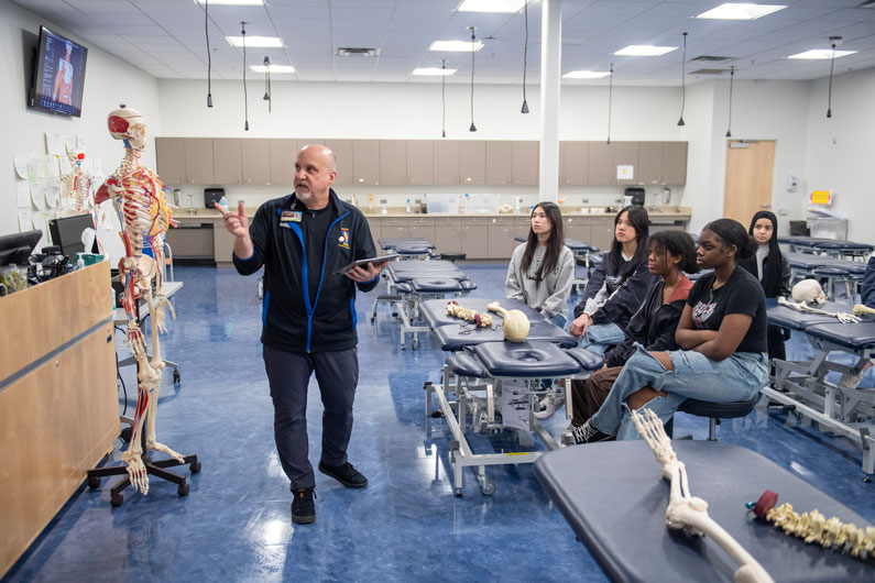 High school students listen to professor teach in front of skeleton anatomy model