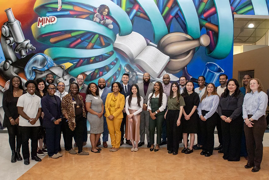 PharmD students and PCOM alumni pose for a picture in front of a wall-sized mural