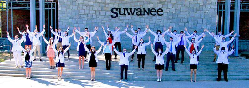 PCOM Georgia physical therapy students pose outside donning their white coats while wearing masks and keeping distance