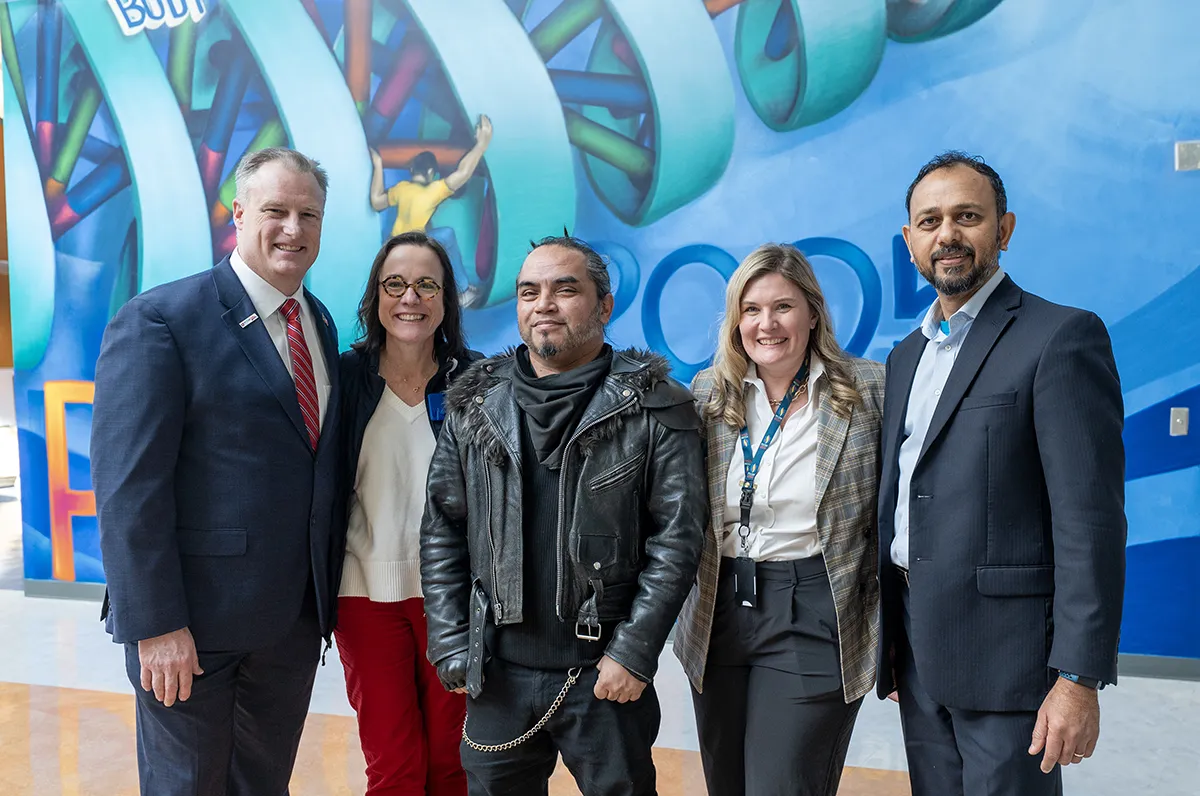 PCOM Georgia administrators and staff smile in front of the new mural art wall alongside artist Mr. Totem