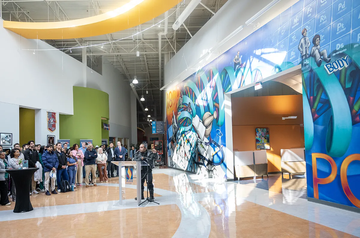 Atlanta artist Mr. Totem speaks at a podium in front of his latest mural at PCOM Georgia