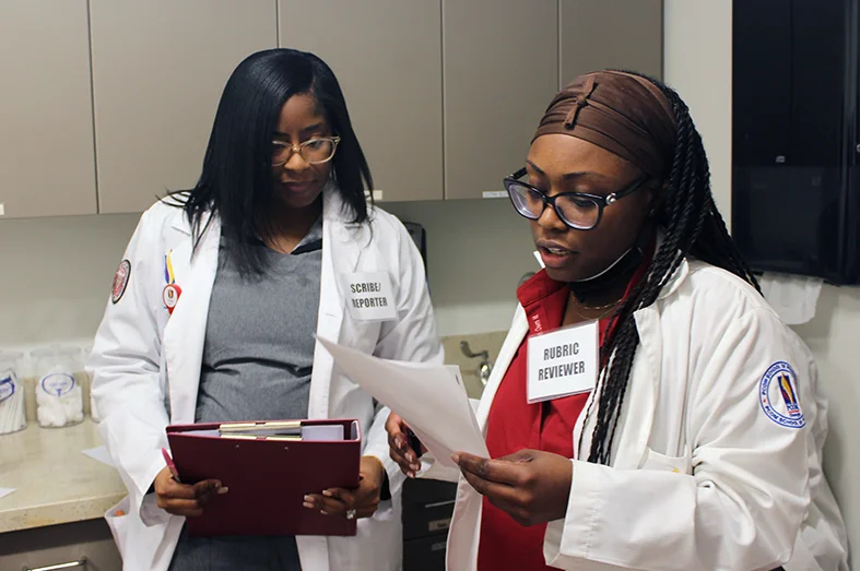 Two PharmD students work with a standardized patient during a scenario-based learning session