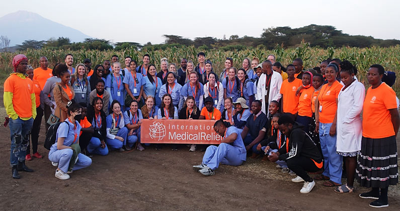 PCOM Georgia students and Tanzanian providers pose outside with an International Medical Relief banner