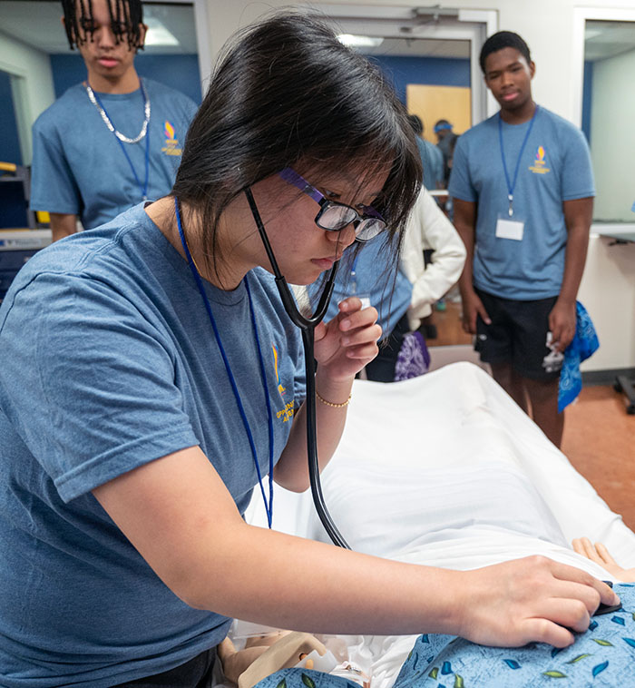 High school student uses a stethoscope to examine a patient simulation mannequin at PCOM Georgia's summer STEM camp