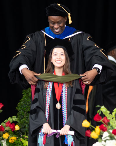 A PCOM Georgia graduate is hooded on stage