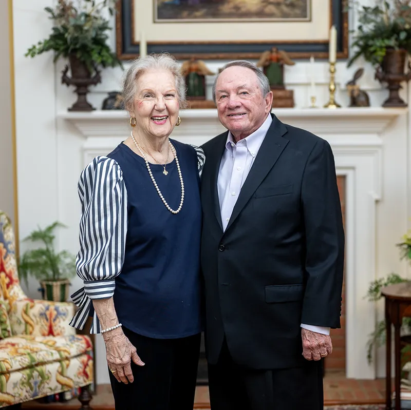 Gwinnett County philanthropists Sandra and Clyde Strickland smile in front of a furnished living room and fireplace in their home