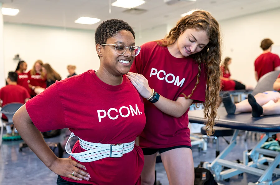 Two PCOM Georgia physical therapy students smile while working on a hands-on training exercise