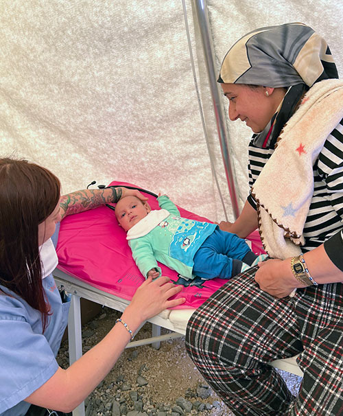 PCOM medical student kneels over and treats an infant earthquake survivor in Turkey
