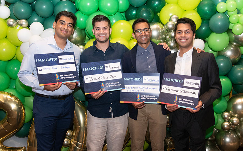 Four PCOM Georgia doctoral students smile and hold their residency match signs in front of balloons