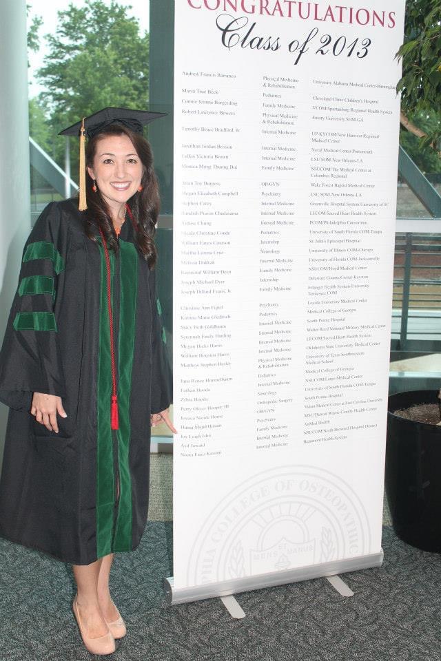 PCOM Georgia's Dr. Zarandy in graduation garb standing next to a large sign with the list of DO Class of 2013 graduates.