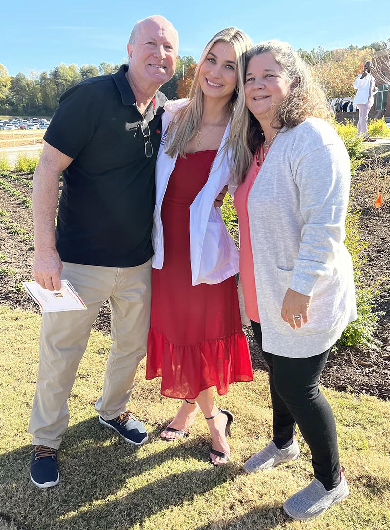 PCOM Georgia med student and urology match Elizabeth DeSellier (DO '26) smiles in her white coat with her parents
