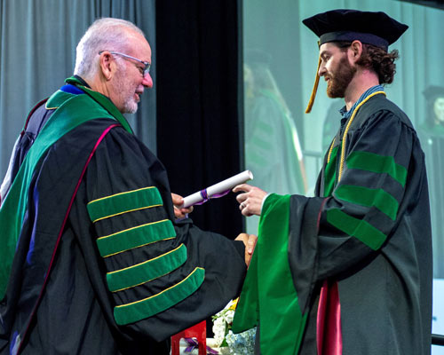 President Jay S. Feldstein, DO ’81, presents diploma to student on stage at commencement ceremony