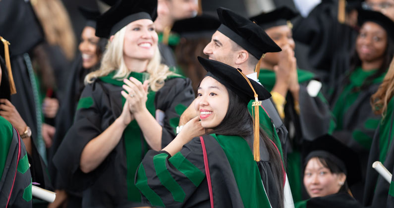 Students wearing graduation robes and caps applaud in an auditorium