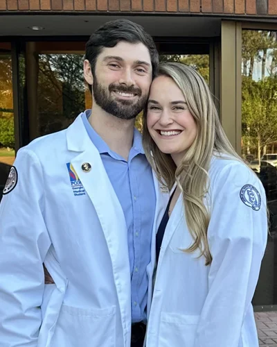 Daniel and Lizzy Burke wearing white coats outside of the PCOM Georgia main entrance