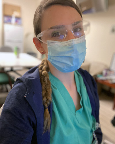 Morgan Fuller (DO '21) wears scrubs, goggles and a surgical mask in a hospital office.