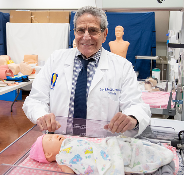 Gary Freed, DO, smiles over an infant mannequin in PCOM Georgia's Simulation Center